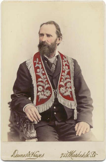 Man posing for a portrait, wearing a red embroidered vest.